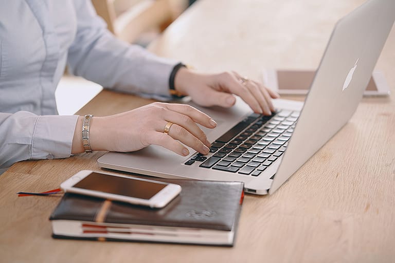 A laptop, sitting on a desk, and being typed on but what appears might be a woman's hands.